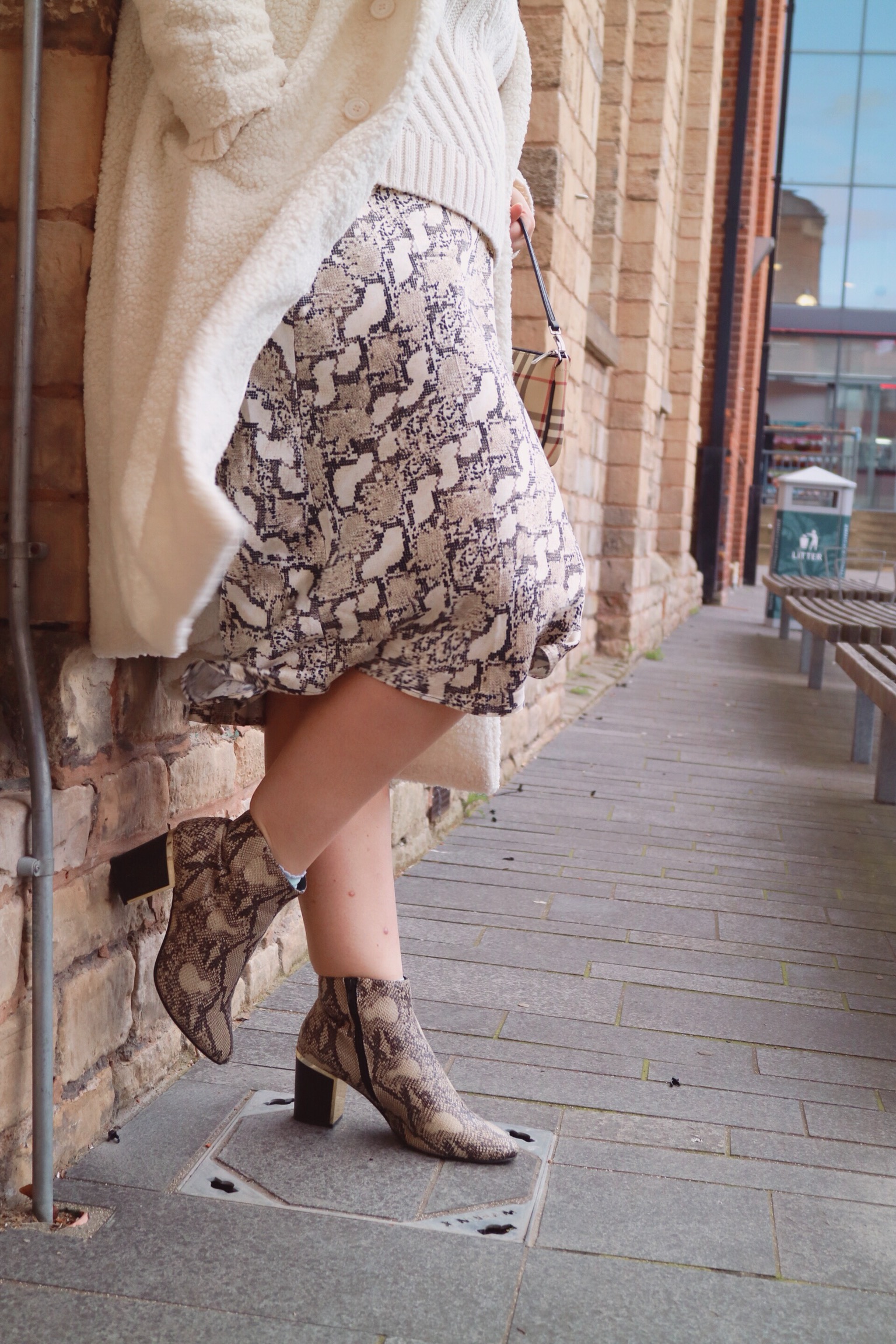 close up of a snake print satin skirt paired with a cream coat and snakeskin ankle boots