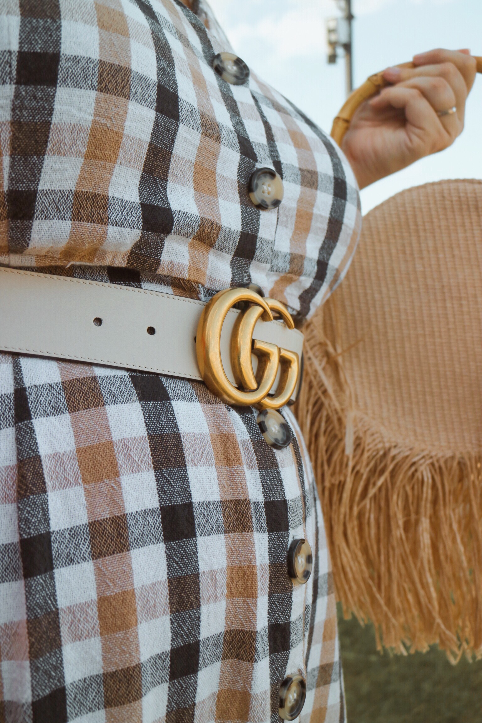 Gucci Belt White GG logo against a check dress and straw bag
