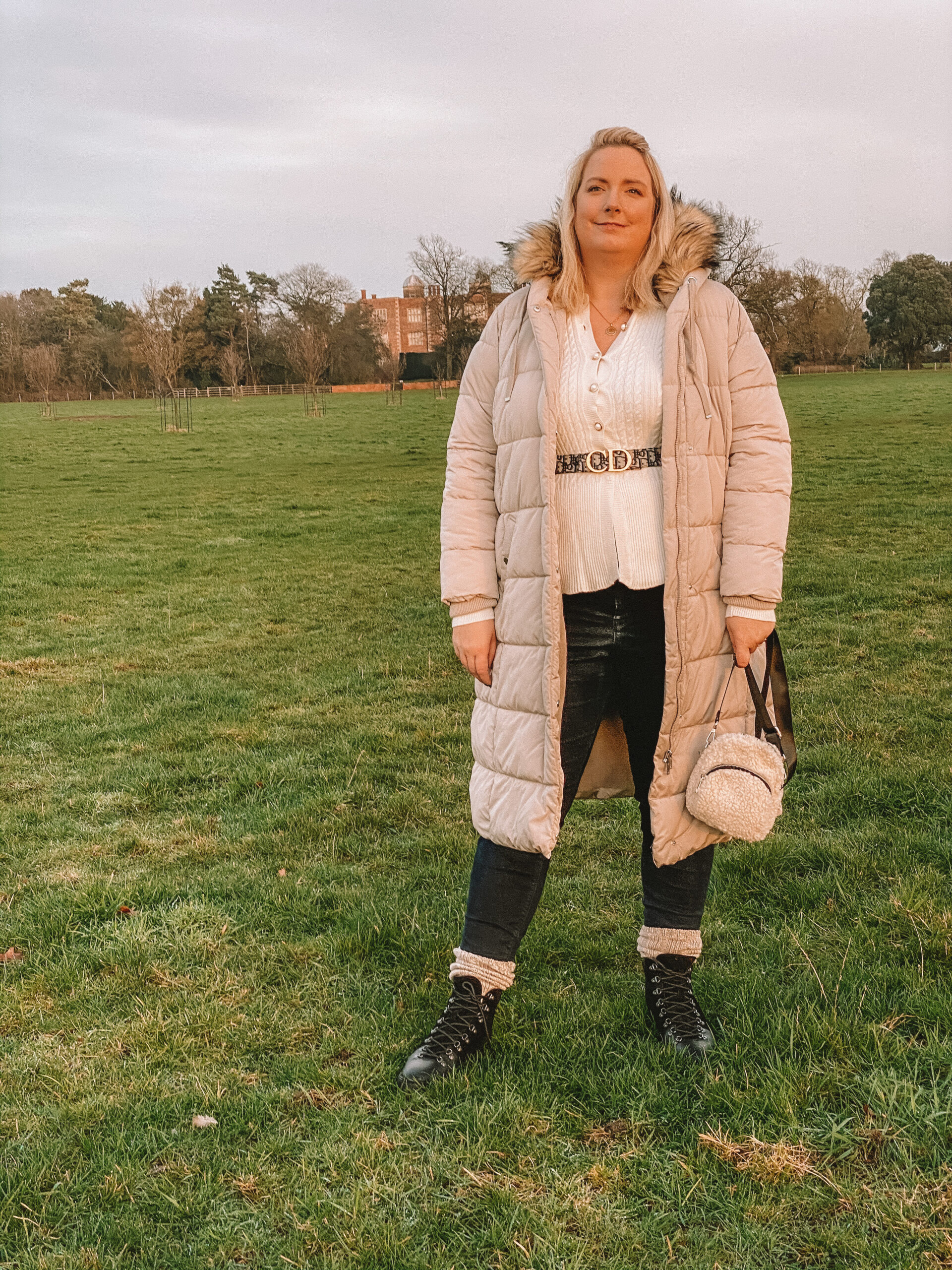 lucy in a field with hiking boots a big coat and the dior plus size belt over a cardy