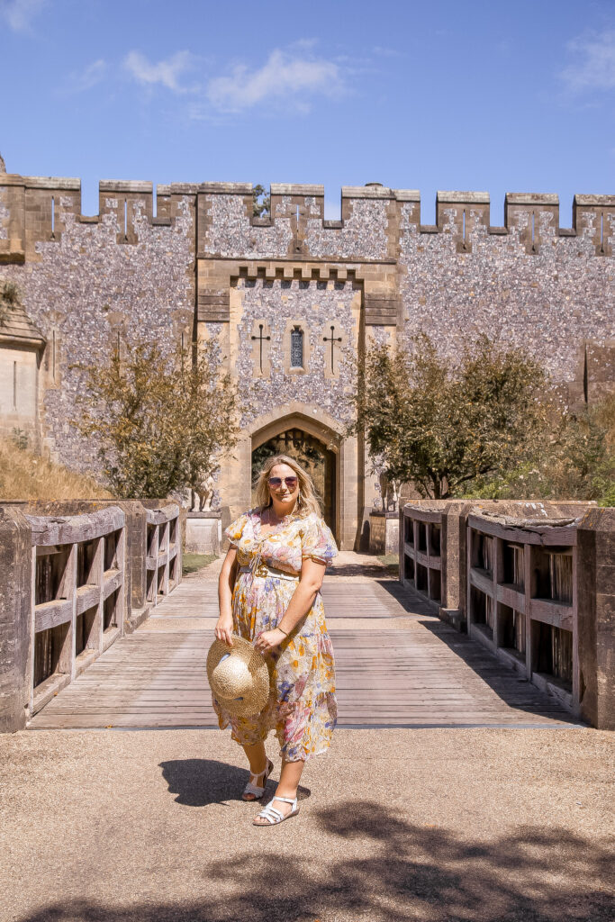 lucy in a plus size neon rose pastel floral maxi dress holding a straw had stood in front of a bridge over the moat and castle walls behind