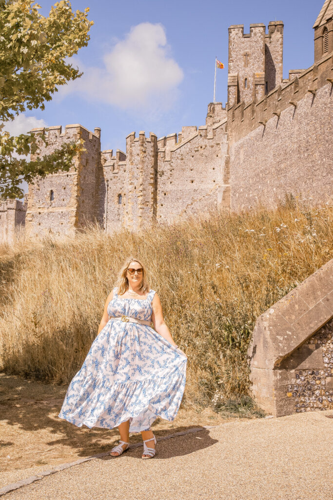 lucy is swishing her blue and white maxi dress and is stood in front of the castle walls