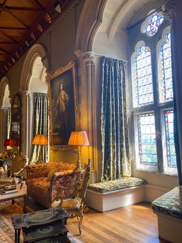 large stained glass windows, bench seats and ornate painitngs and furniture in a room inside the castle