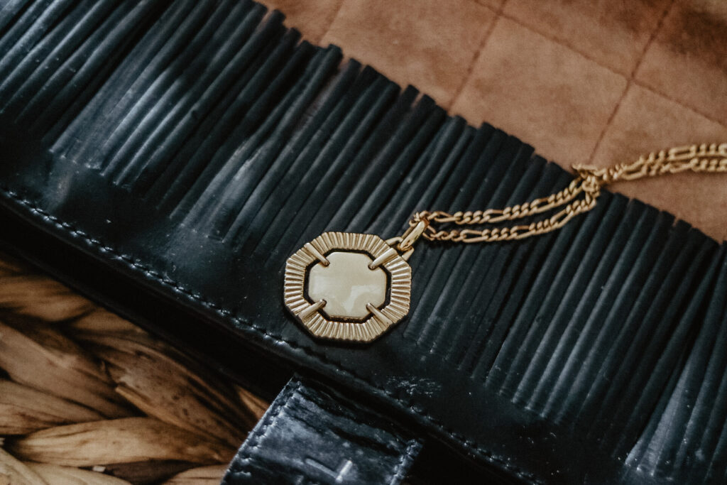 Gold hexagon necklace on top of a hand bag